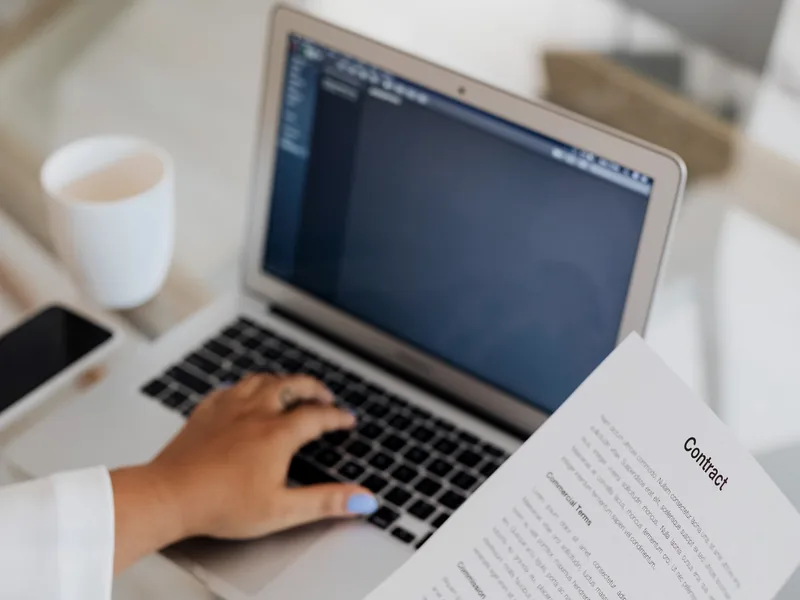 Person holding a document while working on a laptop