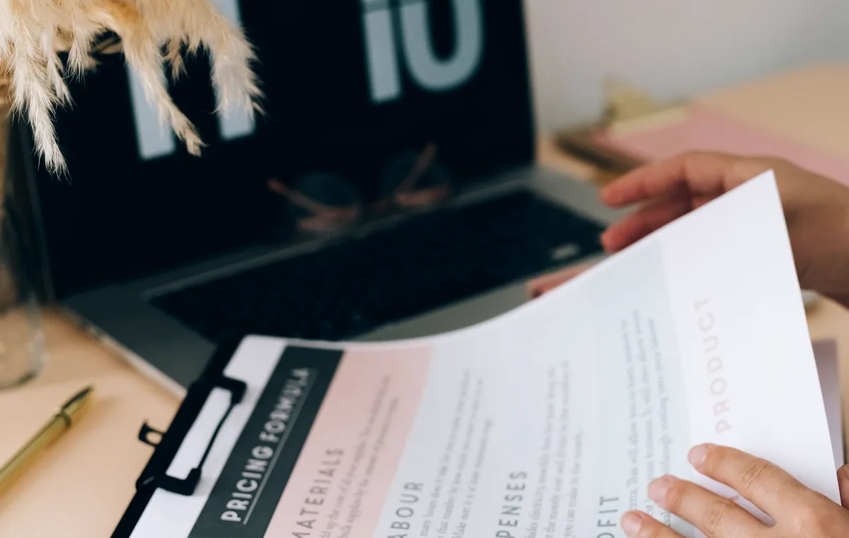 Hands reviewing documents on a desk beside a laptop